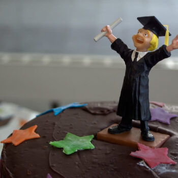 A figure of a man in a graduation cap and gown standing on top of a cake with stars.