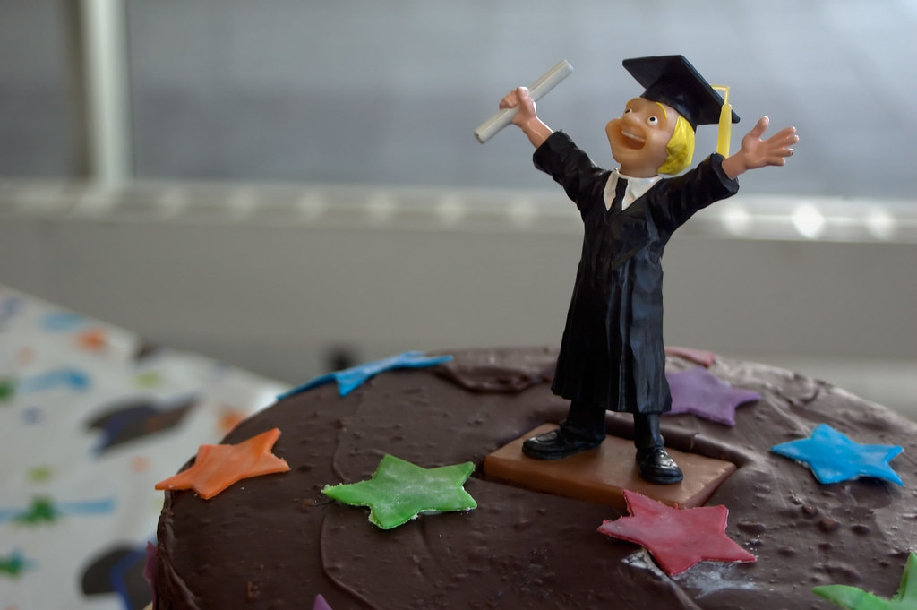 A figure of a man in a graduation cap and gown standing on top of a cake with stars.